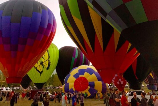 A crowd gathers bneath a bunch of hot air balloons