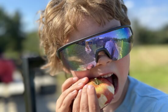 A kid bites an apple in the middle of a field