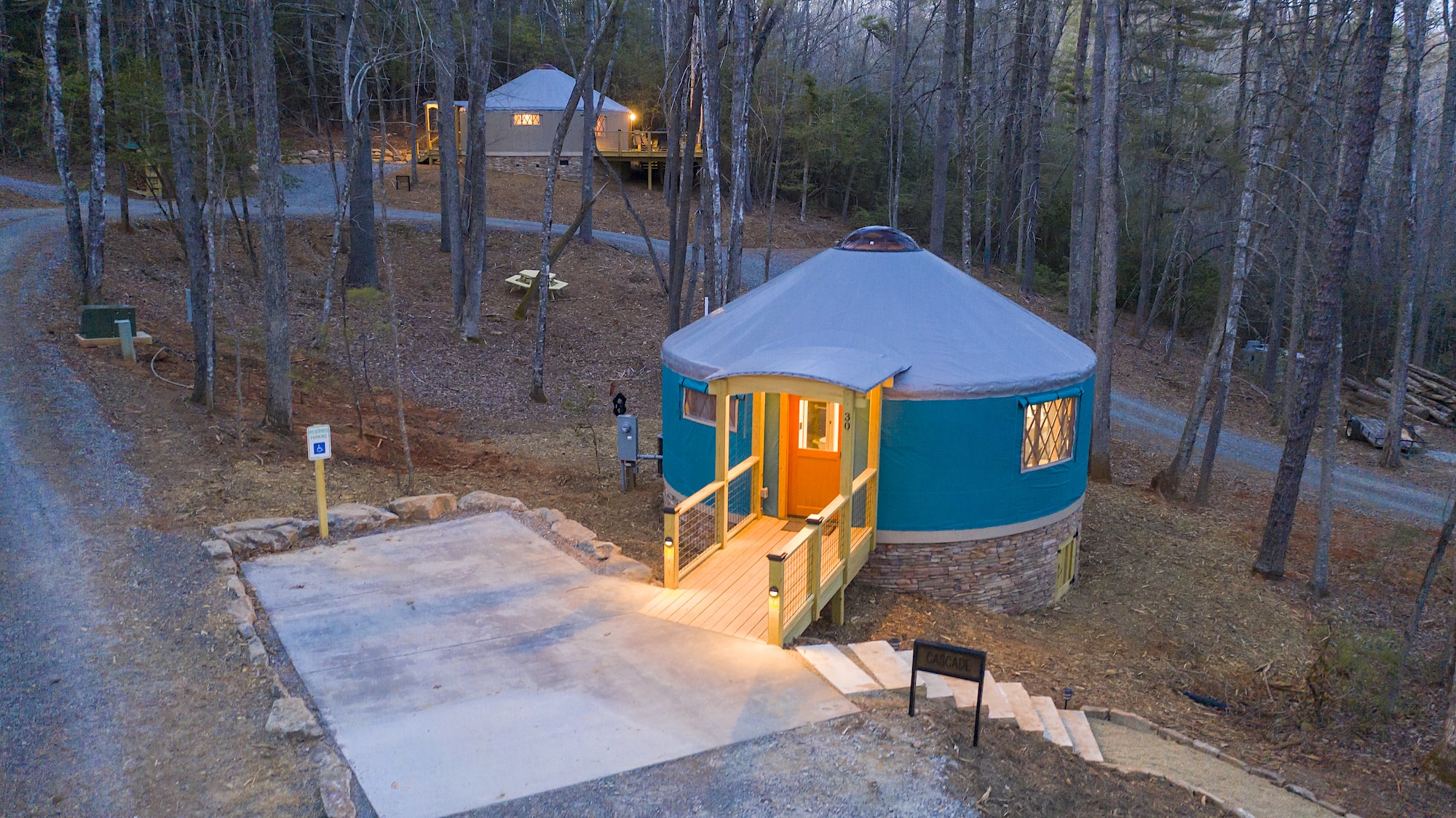 A yurt sits in the woods at night with its lights on