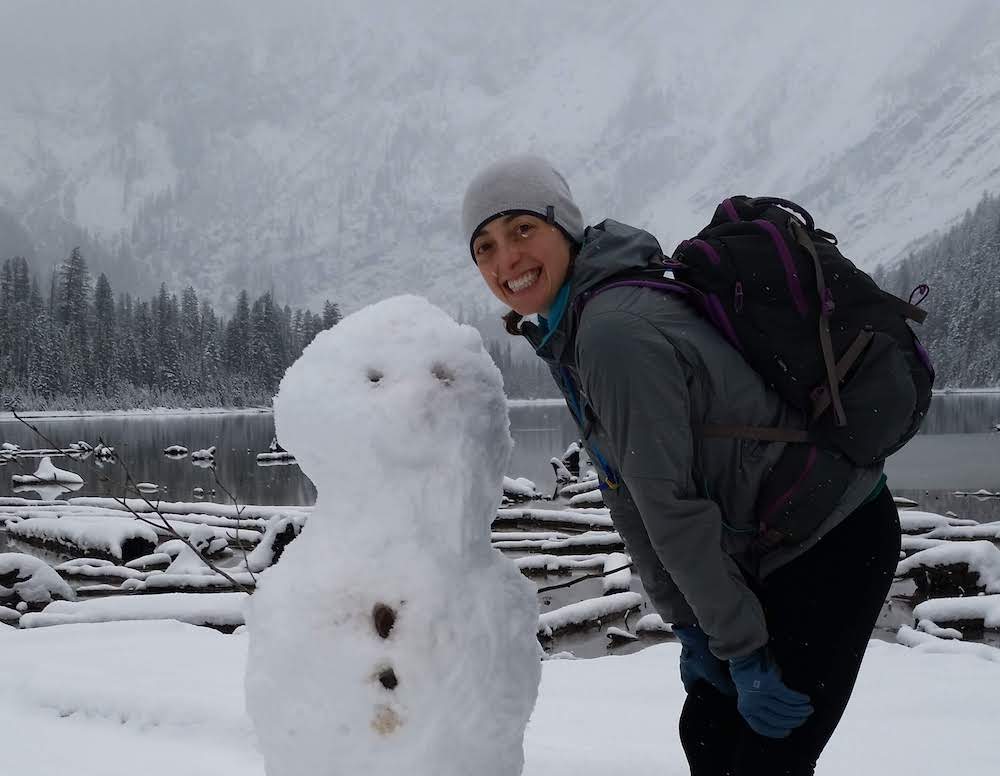 The writer stands next to a snowman in the winter